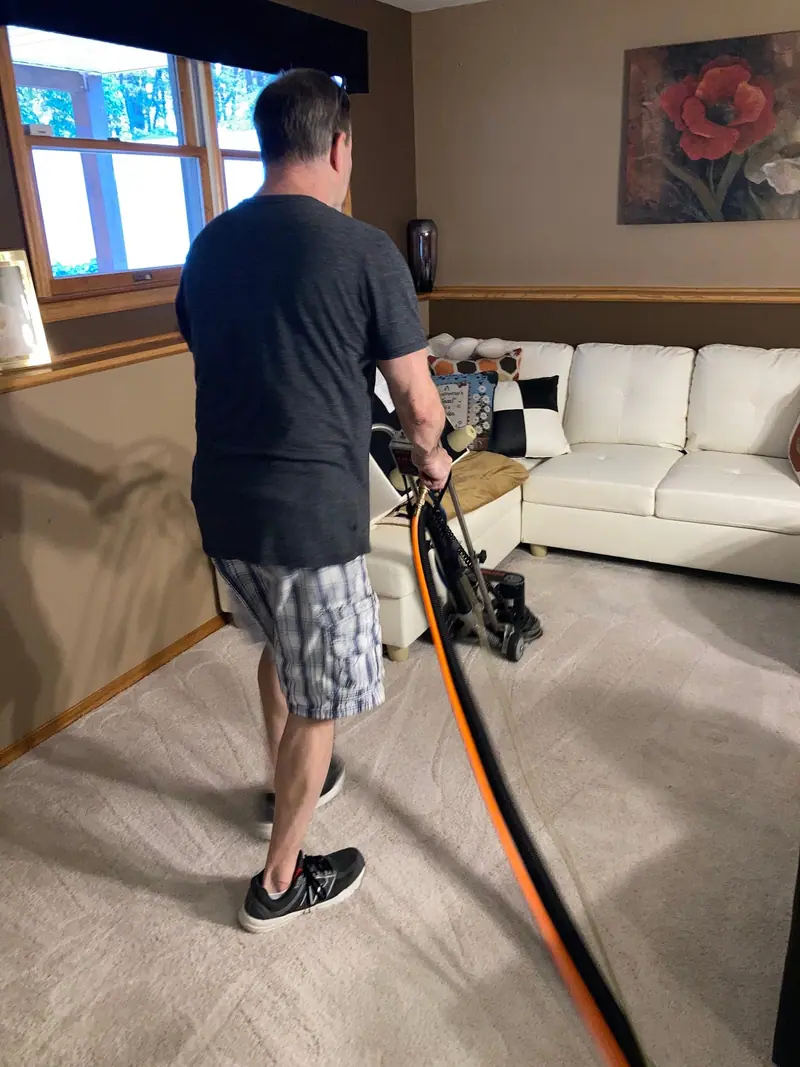 Miracle Men technician running the Rotovac across living room carpet beside a white sectional