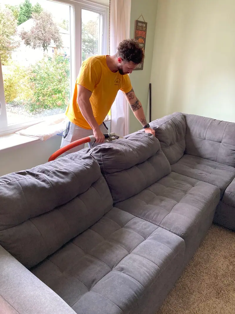 Technician cleaning a grey fabric sectional sofa